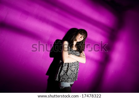 Worried young woman with arms crossed against pink wall with strong shadow. Sad girl in depression concept