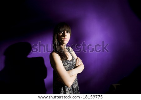 Worried young woman with arms crossed against purple wall with strong shadow. Sad girl in depression concept