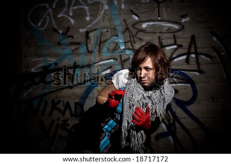 Young woman in dark location with graffiti background wall. Hard light from above