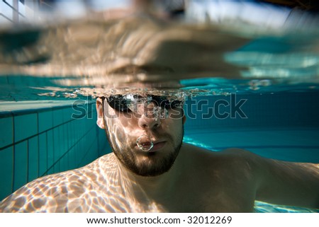 Underwater man portrait with swimming goggles and air bubbles in pool