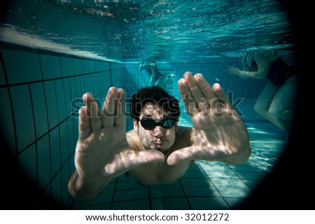 Underwater man portrait with swimming goggles and swimmers in background