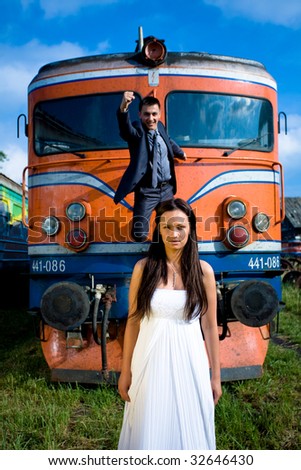 Husband in superman pose on old train and bride in front