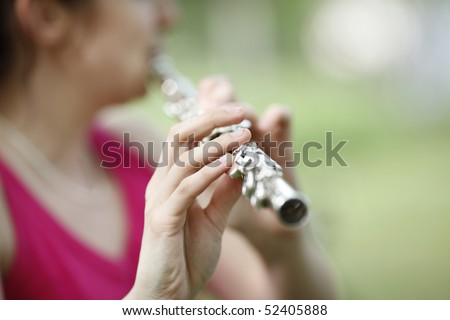 Young woman playing classic flute in nature in background. Shallow DOF