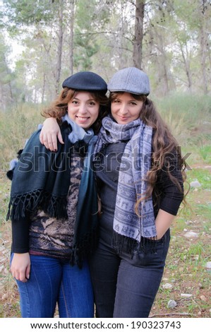 Happy female friends with hats and scarfs in a forest, hugging
