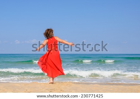 Beautiful lady in bright elegant red dress  at beach, with sea and blue sky as background