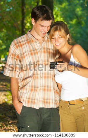Young couple looking at cell phone happily while relaxing in nature