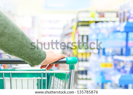 Close up of women hand pushing shopping trolley in supermarket, focus on hand