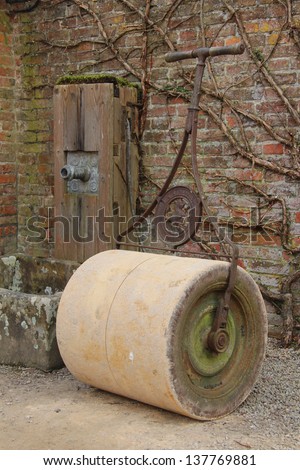 Old garden roller and water pump in an English country walled garden.