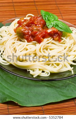 Italian dinner: spaghetti. Macaroni with tomato sauce with garlic, olives and fresh basil isolated on green leaf.