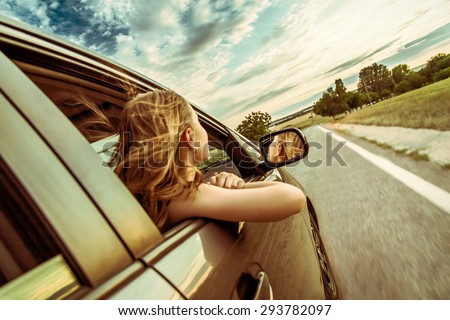 Happy beautiful girl traveling in a car across Europe with focus in front of the car
