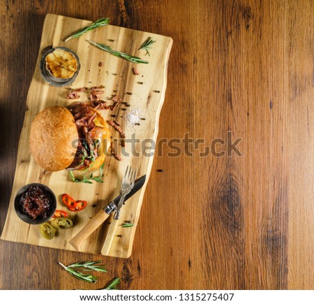Homemade beef burger with crispy bacon and vegetables on rustic serving board
