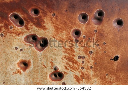 background - side of a rusting metal fridge with bullet holes