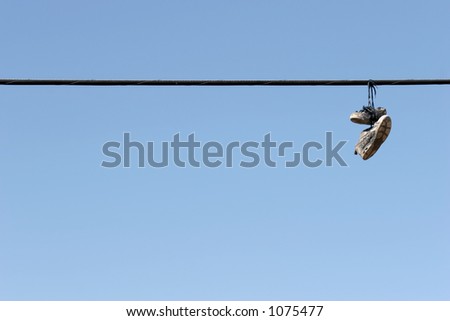 shoes on power lines - urban scene, worn tennis shoes hanging from a power line against clear blue sky. plenty of copyspace.