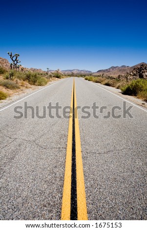 road trip through joshua tree national park, california. straight stretch of road with blue sky and copyspace