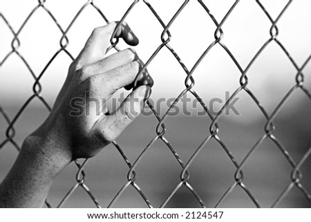 depression - close up of hand on chain-link fence. Limited depth of field, converted to black and white with added grain.