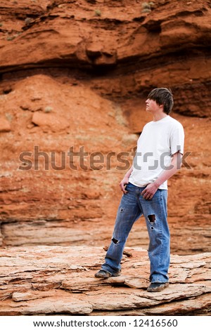 teenager standing on a rock in the mountains of wyoming. Muddy shoes, holes in jeans, hands in pocket.