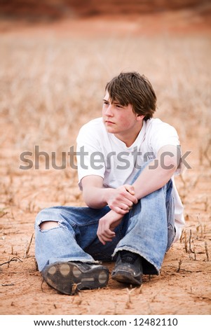 teenager sitting amongst the weeds in a dry lake bed. Natural-looking teen, simple clothing, ripped jeans, shot in Wyoming with copyspace.