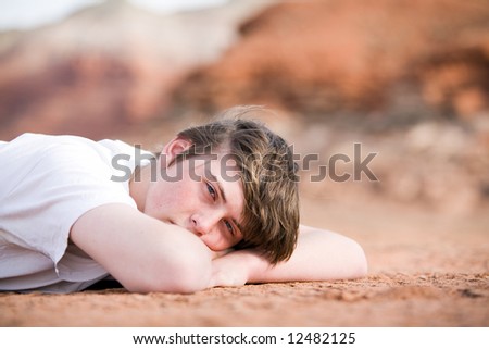 teenager male laying on the ground outdoors, natural light with mountains in background
