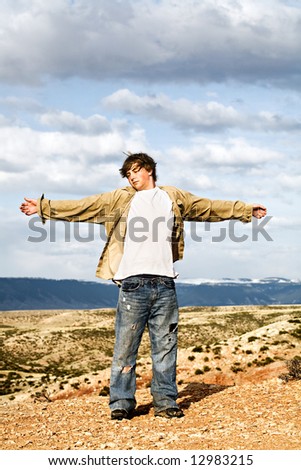 teen male standing in the wind on the edge of a cliff, arms wide open
