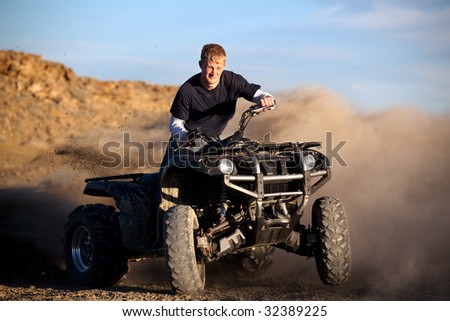 male teenager riding a quad 4x4 - kicking up dust with his four wheeler