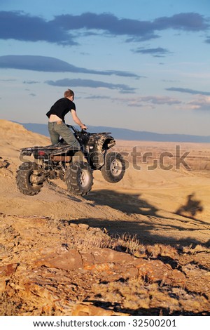 Teenager jumping on a quad ATV in late sun - four wheeler getting air in the hills of Wyoming