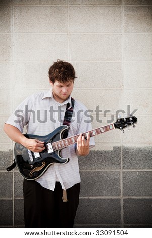young man playing his hollow-body guitar - outdoors against wall