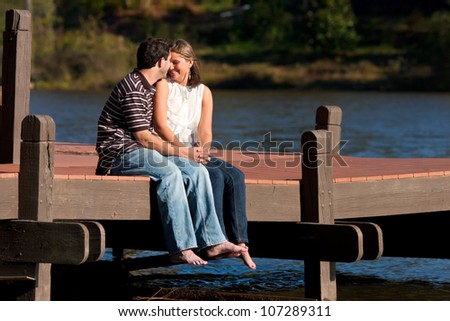 Young Couple In Love Sit Barefoot On Dock