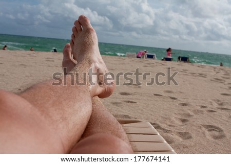 A man\'s sandy legs stretch out on a lounge chair on Ft. Lauderdale beach