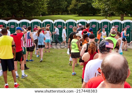 ATLANTA, GA - JULY 4: Exhausted runners wait in long lines to use a Johnny On The Spot portable toilet, after just completing the Peachtree Road Race 10K on July 4, 2014 in Atlanta, GA.