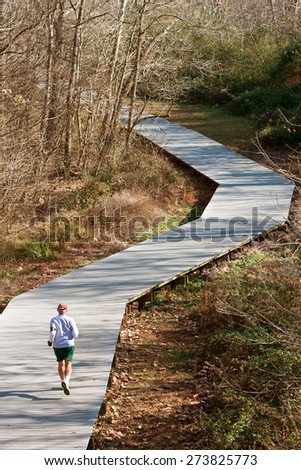 A senior man runs alone along a jogging path made of wooden decking in the middle of the woods.