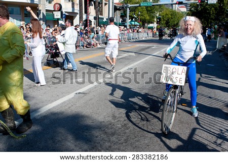 MIAMI, FL - DECEMBER 28:  A senior woman poses as an ebola nurse riding a bicycle while participating in the annual Mango Strut parade in Coconut Grove, on December 28, 2014 in Miami, FL.