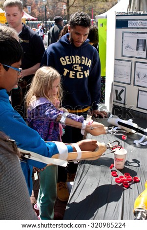 ATLANTA, GA - MARCH 28:   Kids attempt to drop bottle caps into a cup using a prosthetic arm and hooks, at an exhibit at the Atlanta Science Fair in Centennial Park on March 28, 2015 in Atlanta, GA.