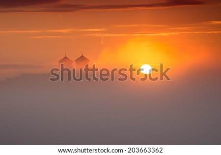 Church towers of the Tyniec abbey in the morning, with the rising sun illuminating the fog