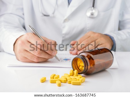Yellow pills on table, doctor writing medical notes in background