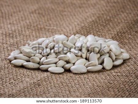 Uncooked white beans on burlap background