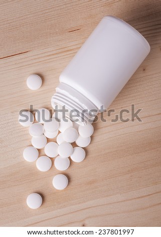White pills spilled from a pill bottle on wooden table.