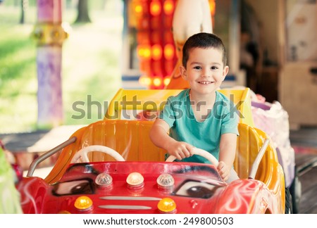 Happy smilling boy driving car toy at an amusement park. Toned photo.