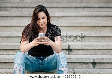 A portrait of a beautiful young woman texting with her phone. Toned photo