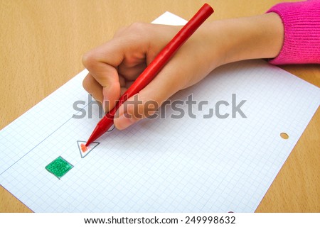 Child drawing a red triangle and a green square with a red wax crayon
