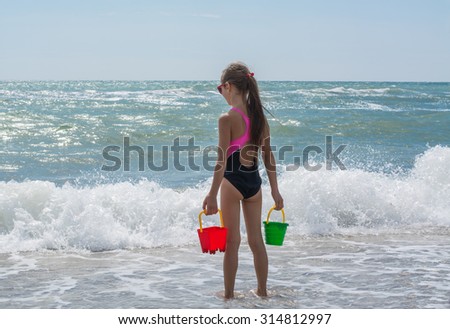 Girl watching the waves from the shore of the sea with toy bucket of water