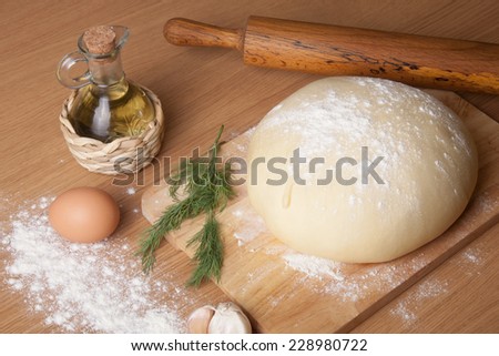 dough on a board with flour. olive oil, eggs, rolling pin, garlic and dill