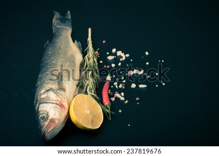 Fresh sea fish lying on dark background with spices. Space for text.tinted