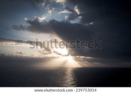 Dramatic sunset rays through a cloudy dark sky over the ocean. Tinted