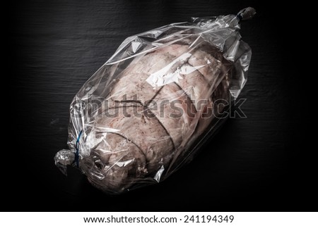 Raw meat with rope in the package on a black background. Toned.