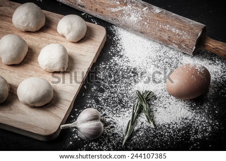 Garlic, rosmary, egg, rolling pin and pieces of dough on the wooden board. Toned.