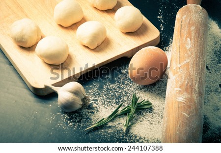 Garlic, rosmary, egg, rolling pin and pieces of dough on the wooden board. Toned.
