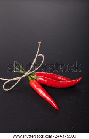 Three red hot chilli pepper with rope on old black background.