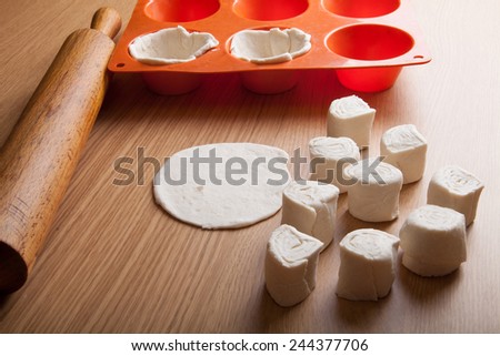 Form for pastry, rolling pin and pieces of dough on the wooden board.