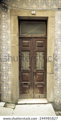 Old wooden door with window on the wall with ceramic tile. Toned.