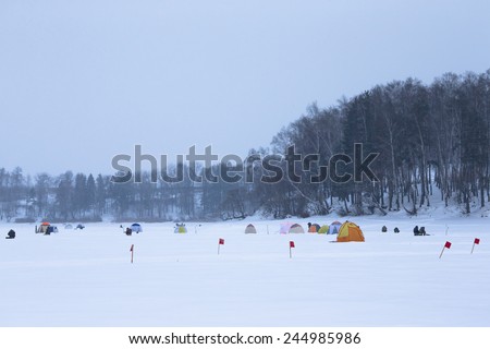 Many flags and tents on the snow-covered field near the forest.
